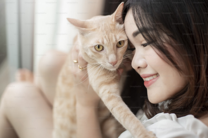 Smiling woman cuddling her light orange cat in a warm, affectionate moment.