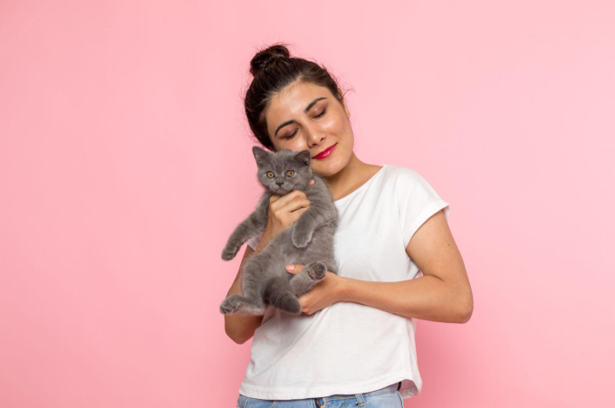 Woman in a white t-shirt holding a grey kitten against a pink background