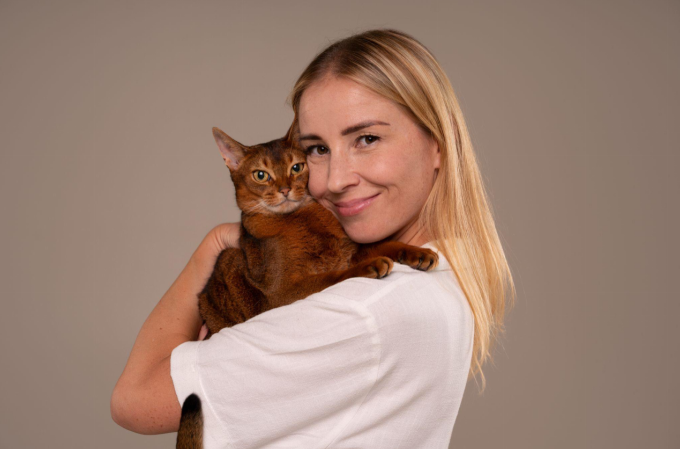 Smiling woman holding a brown cat close to her face.